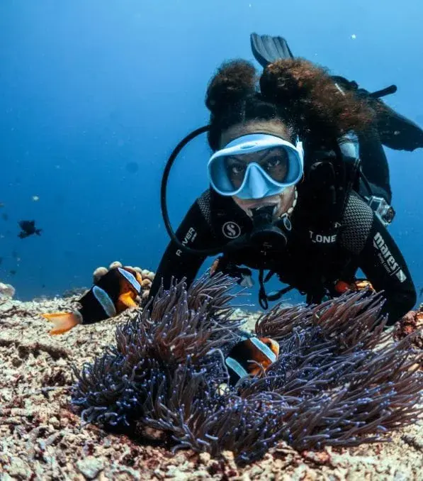 Plongeuse à Nusa Penida observant des poissons-clowns autour d'une anémone sur le récif corallien sous-marin.