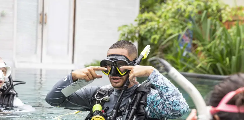 Instructeur de plongée à Nusa Penida ajustant son masque et expliquant une technique à des élèves dans une piscine.