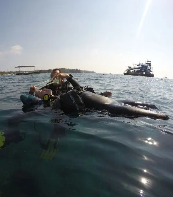 Deux plongeurs en combinaison flottent à la surface à Nusa Penida pendant qu’un instructeur pratique une remontée assistée et lui redonne un détendeur.