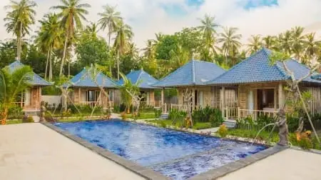 Bungalows en bord de piscine avec palmiers et ciel bleu à Nusa Penida, des vacanciers se détendent autour du bassin.