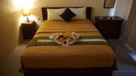 Lit double dans une chambre d'hôtel à Nusa Penida, draps ordonnés avec serviettes pliées en forme de cœur et éclairage tamisé.