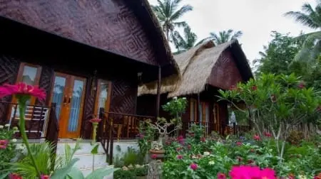 Maisons en bambou au toit de chaume à Nusa Penida, avec terrasse et jardin fleuri au premier plan.