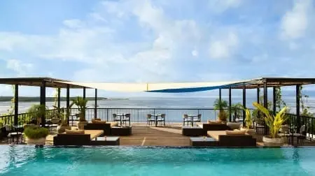 Piscine à débordement avec terrasse lounge et chaises face à la mer, vue panoramique sur Nusa Penida au loin.