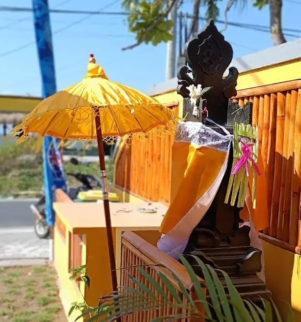 Autel balinais décoré de tissu jaune et d'offrandes sous un parapluie jaune sur Nusa Penida, bord de rue en arrière-plan.