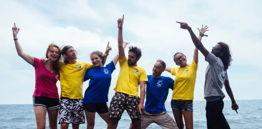 Groupe de sept personnes souriantes levant les bras et posant joyeusement sur un bateau au large de Nusa Penida.