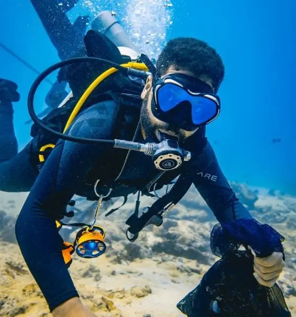 Plongeur en scaphandre ramassant des déchets sur le fond marin de Nusa Penida, masque bleu et détendeur en bouche.