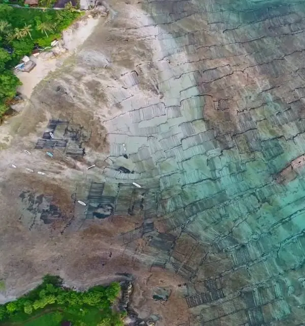 Vue aérienne de Nusa Penida montrant des filets et bateaux sur récif exposé à marée basse, eau turquoise et rive bordée de végétation.